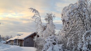Un camino rural cubierto de nieve, con un granero de madera y árboles a ambos lados.