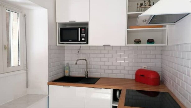A compact kitchen with white cabinets, a black microwave, a sink, and a red storage box. - "La Source", Location Saisonnière Proche Cognac (Cherves-Richemont)