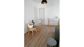 Ett litet, ljust rum med trägolv, ett vitt bord med två stolar, en grå soffa och ett vitt skåp.