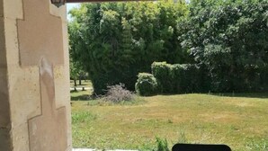 An outdoor patio with a table and chairs, a stone wall, and a view of a grassy area with trees. - "La Source", Location Saisonnière Proche Cognac (Cherves-Richemont)