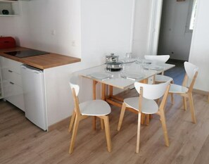 A modern kitchen with a wooden countertop, a built-in dishwasher, and a glass dining table with four white chairs.