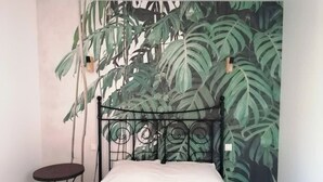 A bedroom with a bed, a small table, and a wall mural of green leaves. - "La Source", Location Saisonnière Proche Cognac (Cherves-Richemont)