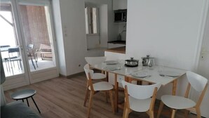 A dining area with a white table and chairs, a kitchen with a microwave, and a sliding glass door leading to an outdoor seating area. - "La Source", Location Saisonnière Proche Cognac (Cherves-Richemont)