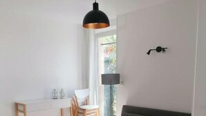 Ett modernt vardagsrum med en grå soffa, ett litet runt bord, en matplats med ett vitt bord och stolar samt ett stort fönster med utsikt över grönområden.