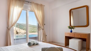 Ein Hotelzimmer mit Bett, Nachttisch aus Holz, Spiegel und Blick auf Pool und Berge.