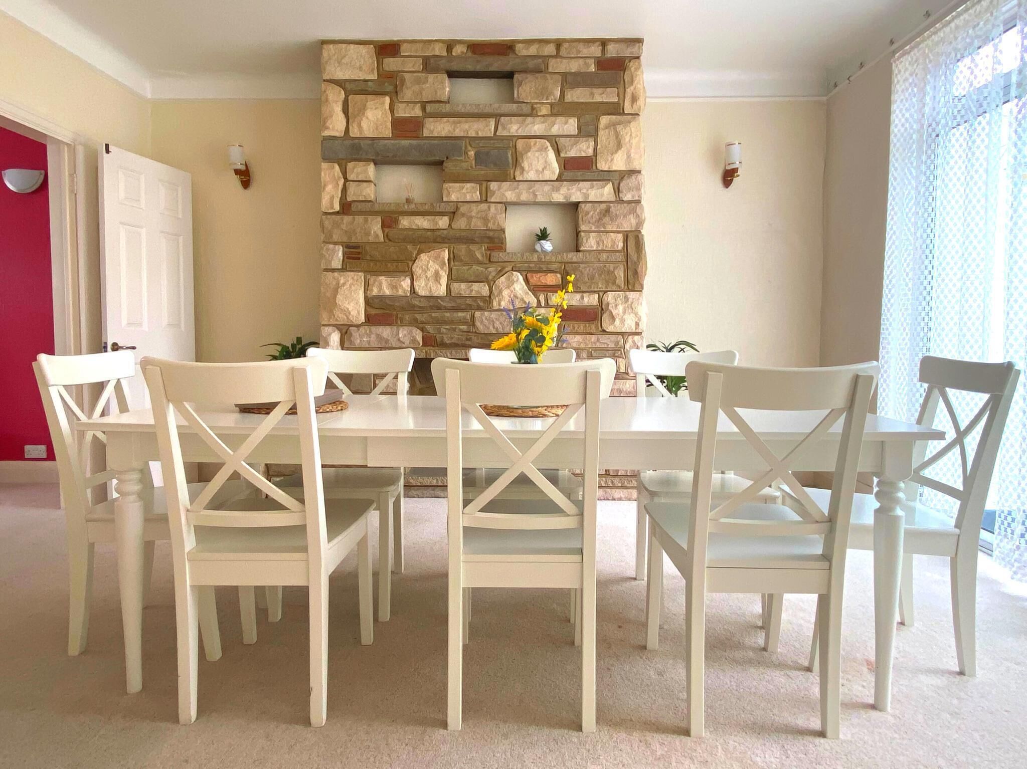 A dining area with a stone wall, white chairs, and a table.