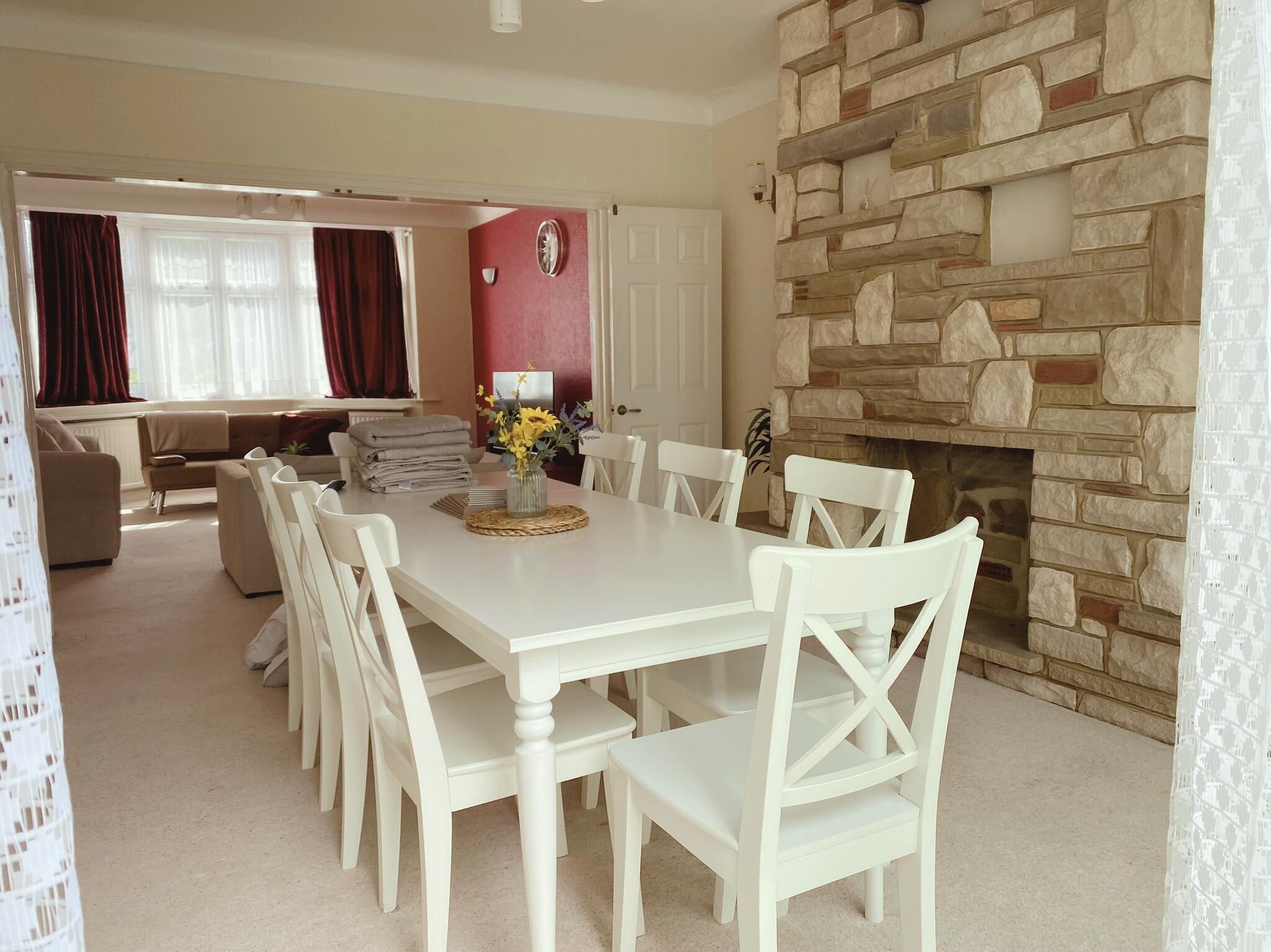 A dining area with a white table and chairs, a vase with flowers, and a stone fireplace wall.