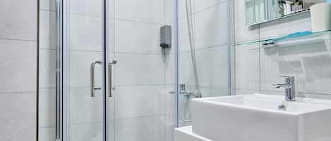 A modern bathroom with a glass-enclosed shower, a white sink, and a mirror above it.