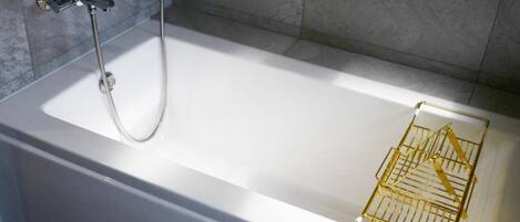 Une baignoire blanche, équipée d’une pomme de douche et d’un porte-serviettes de couleur dorée.