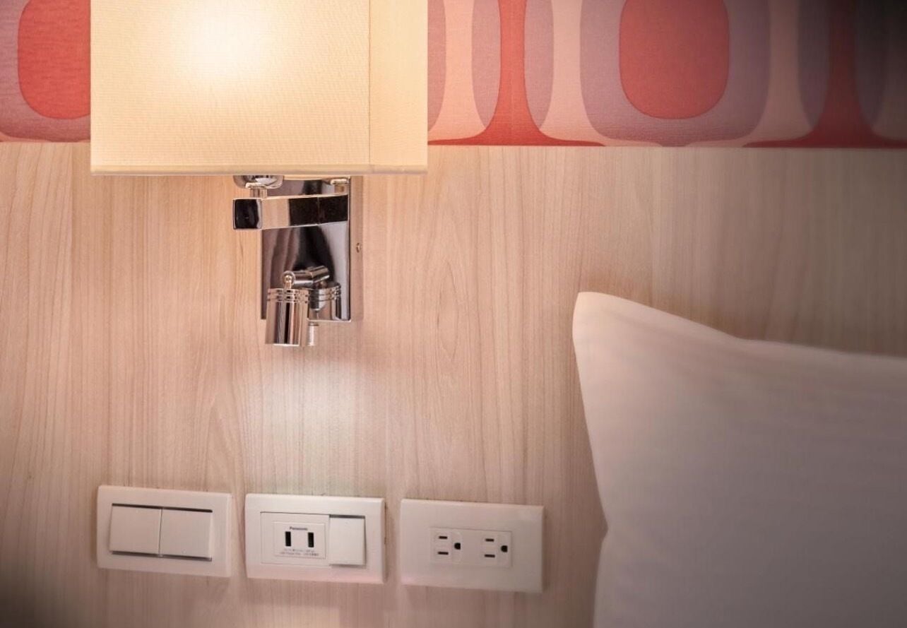 A hotel room with a wooden wall, a light switch, a power outlet, and a small cabinet with a mirror.