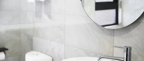 A modern bathroom with a round mirror, a white sink, and a toilet.