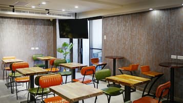 Un espace repas moderne doté de plusieurs tables et chaises, d’un téléviseur à écran plat fixé au mur et d’une grande fenêtre laissant entrer la lumière naturelle.