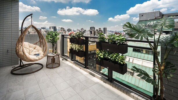 A balcony with a hanging chair, a small round table, and potted plants. - COMMA Boutique Hotel (Taipei)
