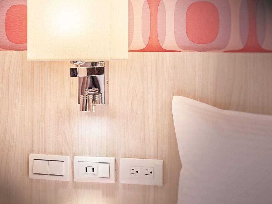 Ett hotellrum med en sänglampa, eluttag och en tidning på nattduksbordet.