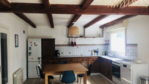 Eine Küche mit Holzbalken, einem Esstisch mit Stühlen, einem Kühlschrank, einem Herd und einem Fenster.