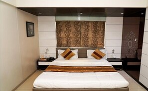 A modern hotel room with a large bed, two bedside tables, a nightstand, and a decorative wall panel. - The Metro Park Hotel (Ahmedabad)