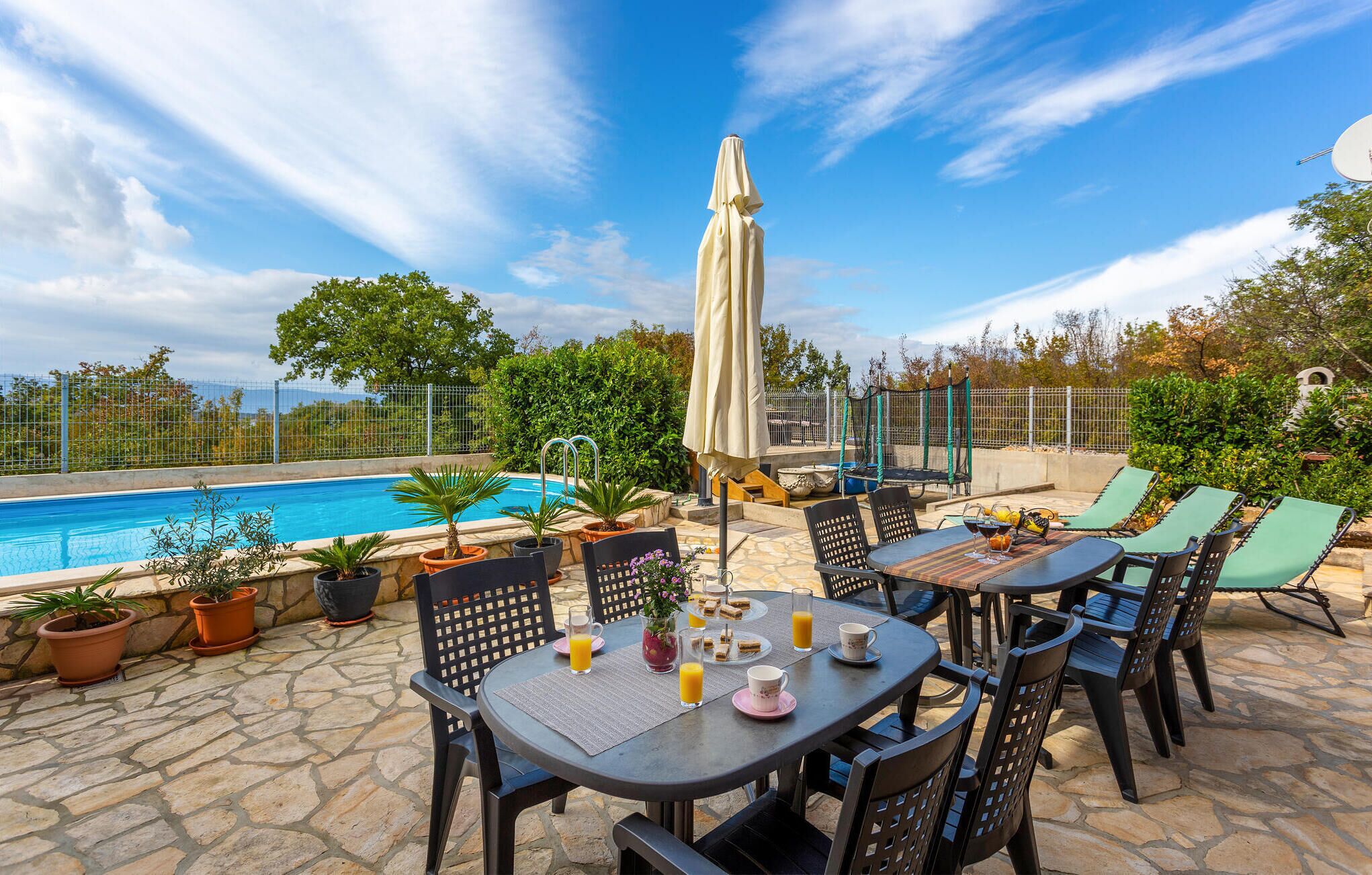 Ein Poolbereich mit Tisch für Zwei, Stühlen und Sonnenschirm.
