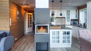 Un intérieur de chalet chaleureux avec une cheminée centrale, des murs en bois et une cuisine moderne.