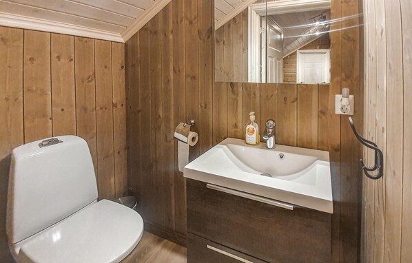 Un baño con paredes de madera, inodoro blanco, lavamanos con espejo y dispensador de jabón.