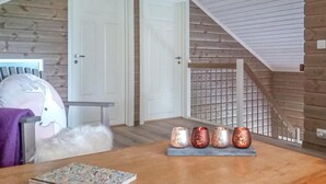 Une pièce aux murs en bois, avec une porte blanche, un escalier et une table sur laquelle sont posées quatre bougies.