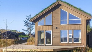 Une maison moderne à deux étages, construite en bois, dotée de grandes fenêtres et d’un toit végétalisé.
