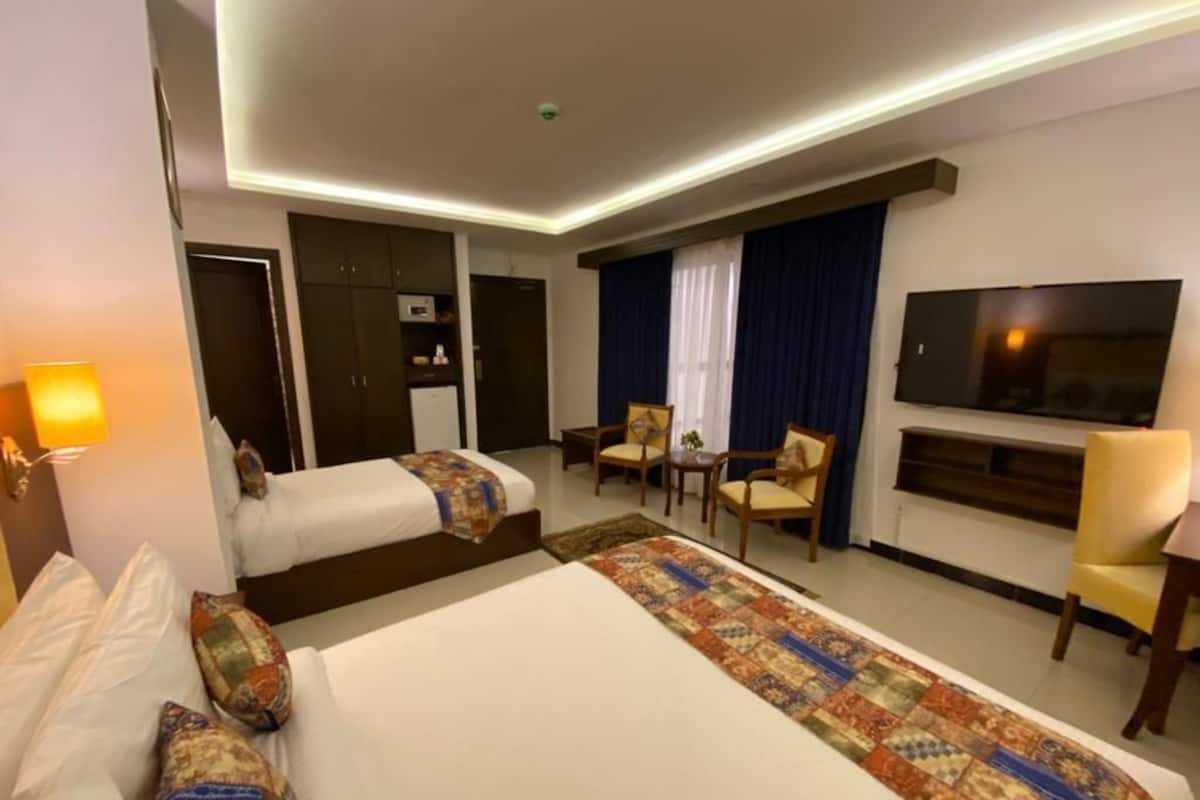 A hotel room with two beds, a TV, a desk, and a chair.