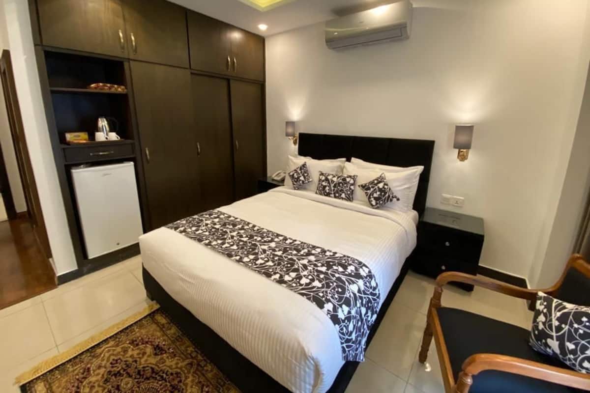 A modern hotel room with a large bed, dark wooden wardrobe, and a small desk with a chair.