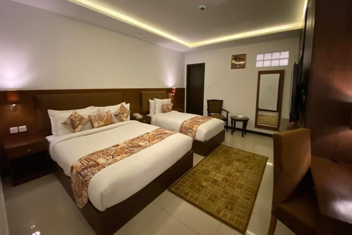 A hotel room with two beds, a sitting area with a chair, a small table, and a mirror on the wall.