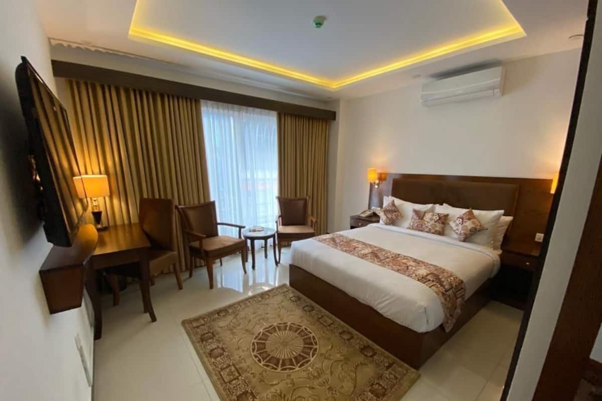 A hotel room with a large bed, a desk with a chair, a TV, and a window with curtains.