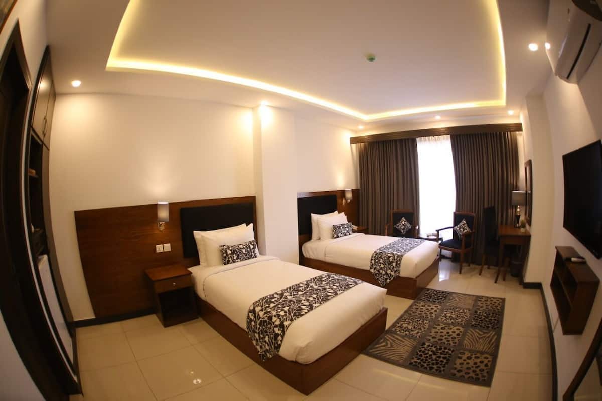 A hotel room with two beds, a desk, a chair, a TV, and a patterned rug.