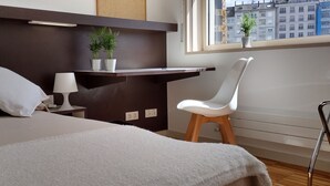 A modern hotel room with a bed, a desk, a chair, and a window with a city view. - Hospedería San Froilan  (Lugo)