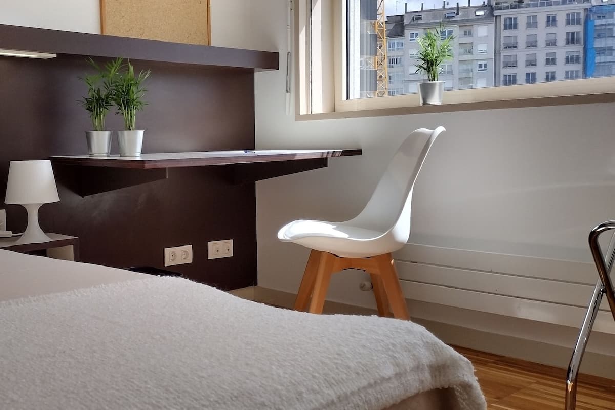 A modern hotel room with a bed, a desk, a chair, and a window with a city view.