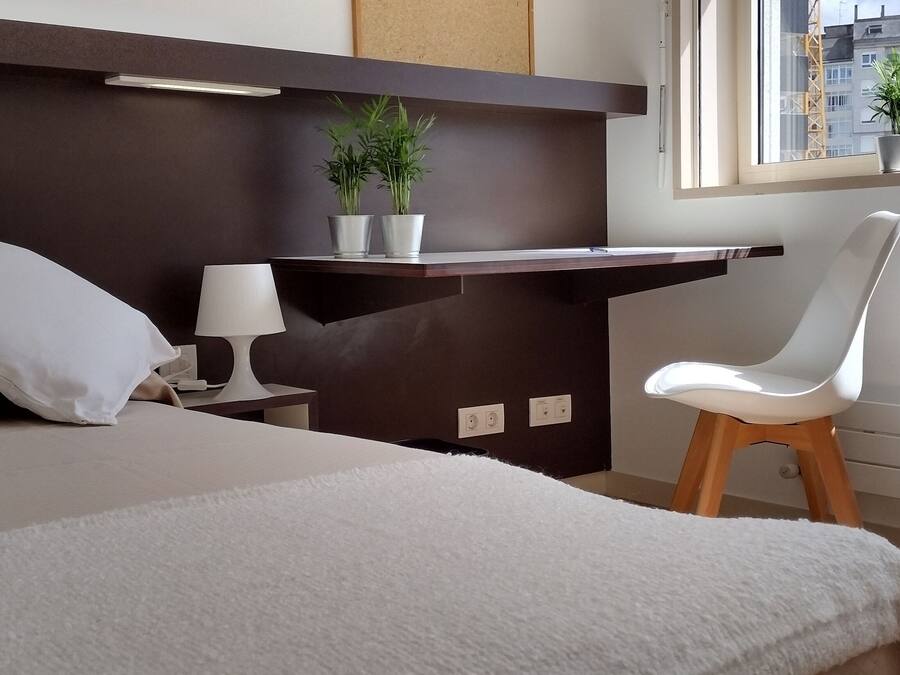Et moderne hotelværelse med seng, skrivebord, stol og et vindue med udsigt over byen.