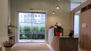 A reception area with a glass door leading outside, a reception desk, a potted plant, and a seating area with a magazine on the table. - Hospedería San Froilan  (Lugo)