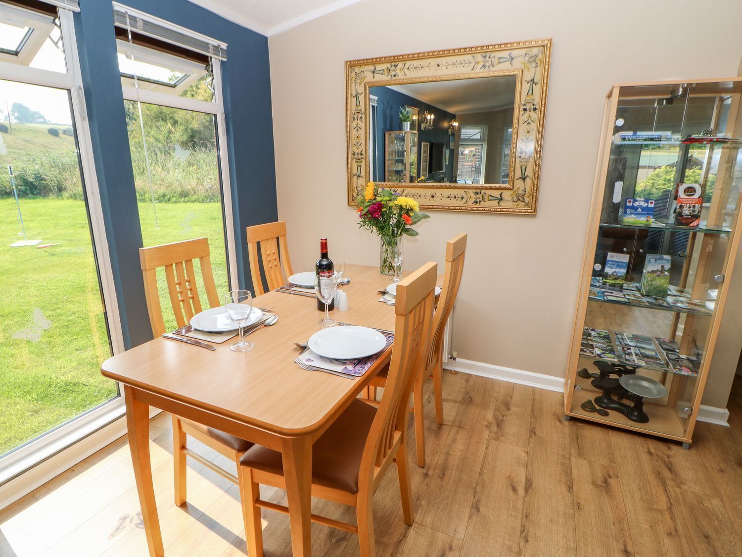 A dining area with a table set for four, a wine bottle, and a vase with flowers.