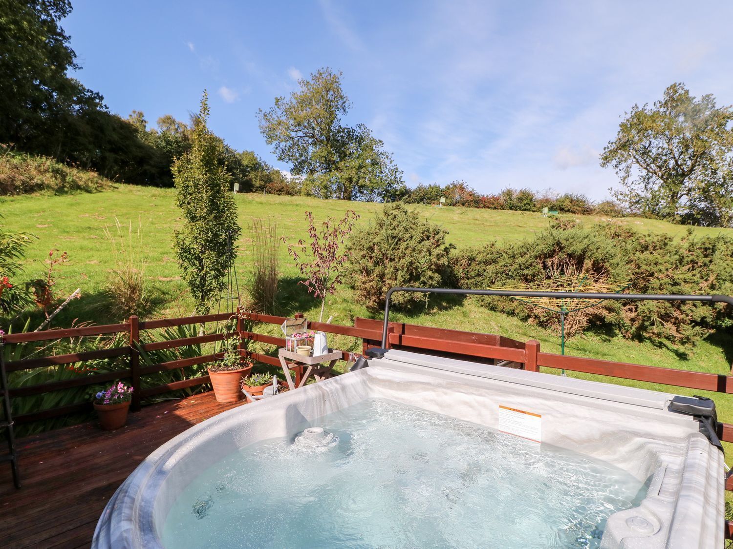 Ein Whirlpool auf einer Holzterrasse mit Blick auf einen grasbewachsenen Hügel und Bäume.