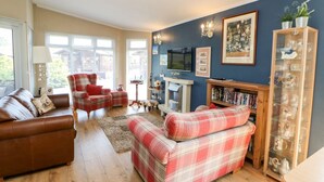A living room with a brown leather sofa, a red plaid sofa, a red armchair, a fireplace, a television, and a glass cabinet with decorative items. - 6 Badgers Retreat (Richmond)
