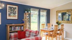 A living room with a plaid sofa, a bookshelf, a dining table with chairs, and a large mirror on the wall. - 6 Badgers Retreat (Richmond)