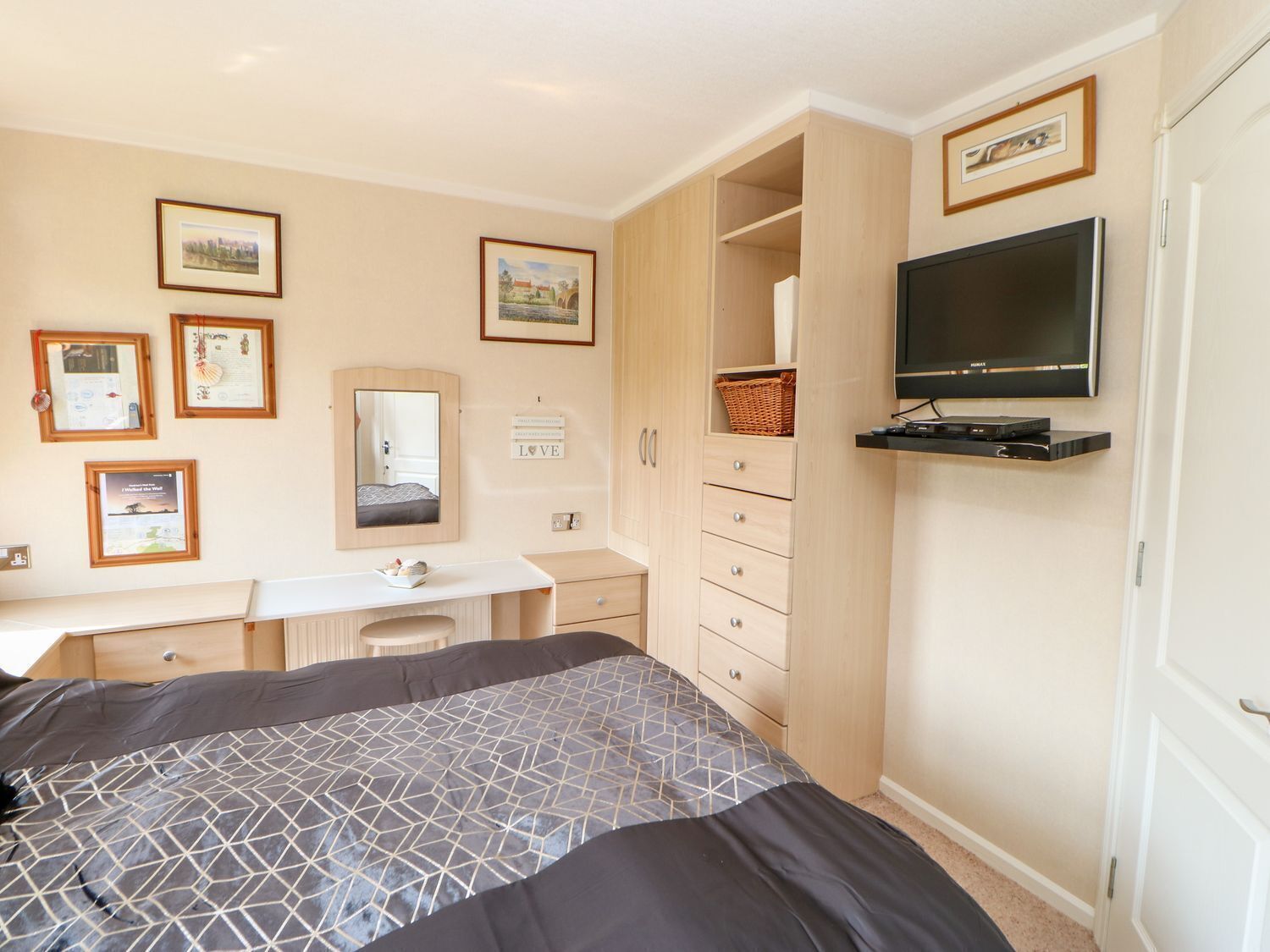 A bedroom with a bed, a desk, a dresser, a TV, and framed pictures on the wall.