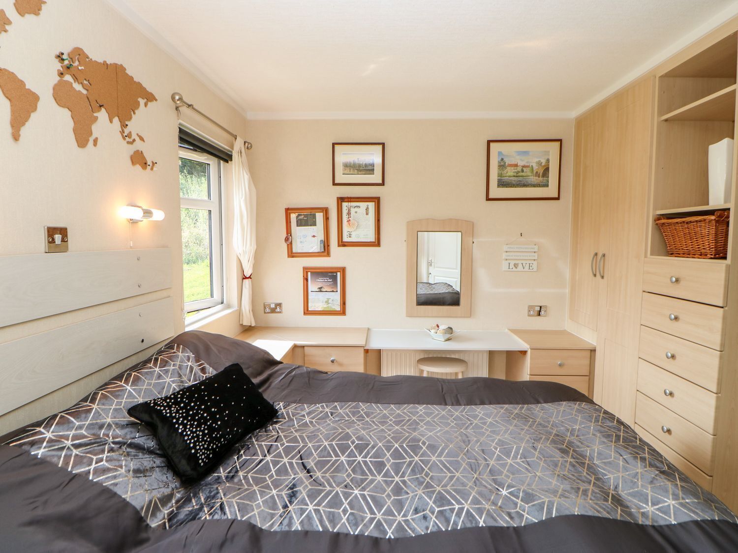 A bedroom with a bed, a desk, a dresser, and a window with a view of greenery.