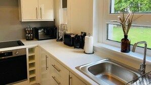 Una cocina moderna con armarios blancos, un lavamanos de acero inoxidable, un tostador y una ventana con vistas a zonas verdes.