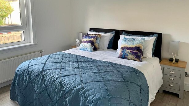 Un dormitorio con cama, dos almohadas, una mesita de noche y una ventana.