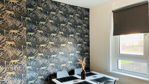 Un comedor con una mesa dispuesta para dos, un papel tapiz de diseño oscuro y una ventana con persiana.