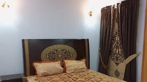 A bedroom with a dark wooden bed frame, a patterned bedspread, and a ceiling fan. - Al-Rehman Palace 1 (Mekhtar)