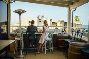 Una pareja cenando en una mesa con vista al mar. Hay sillas, una mesa y una lámpara.
