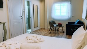 A hotel room with a bed, towels, a desk with a chair, a small table, a sofa, and a window. - Domus Bat Galim Hotel (Haifa)