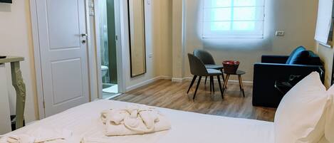 A hotel room with a bed, towels, a desk with a chair, a small table, a sofa, and a window.