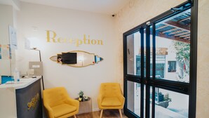 A reception area with a reception desk, two yellow armchairs, a large window, and a wall-mounted TV. - Domus Bat Galim Hotel (Haifa)