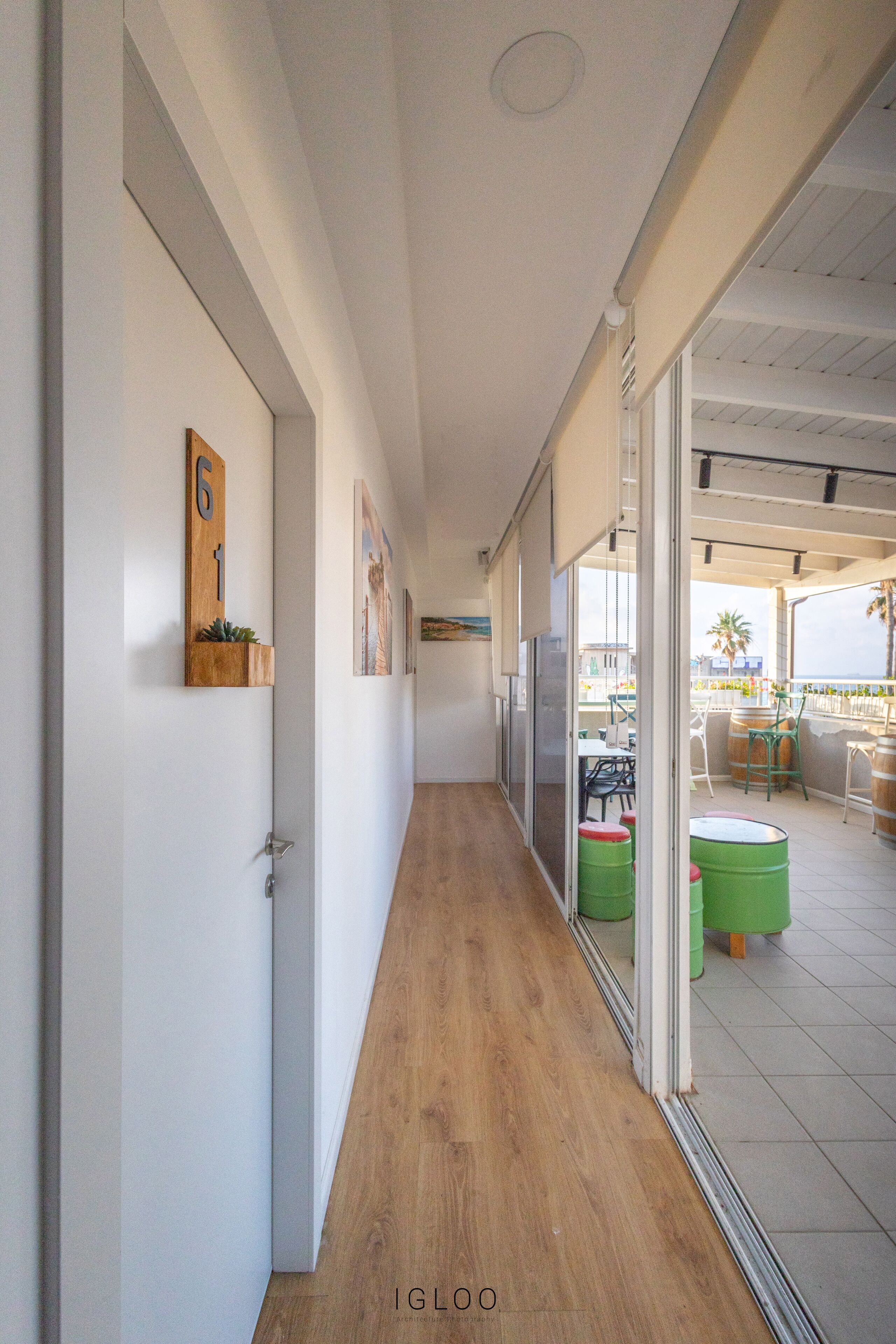 A hallway with wooden flooring, white walls, and a glass door leading to an outdoor seating area with chairs and tables.