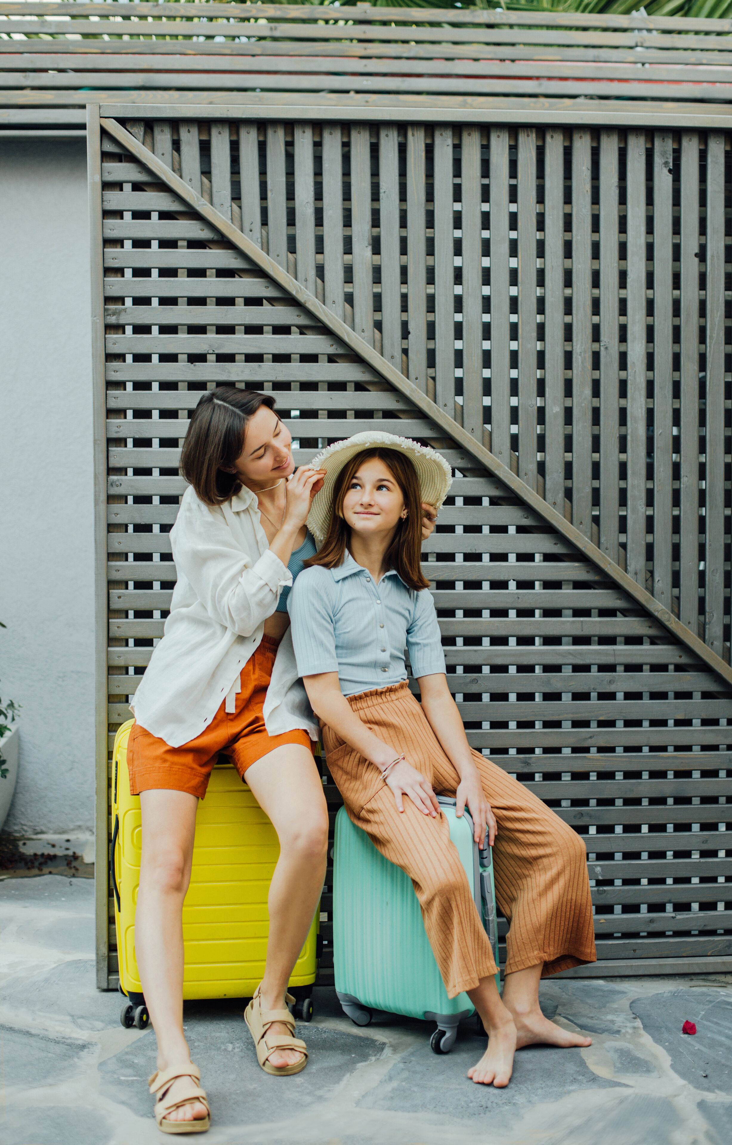 Two people sitting on suitcases against a wooden fence.